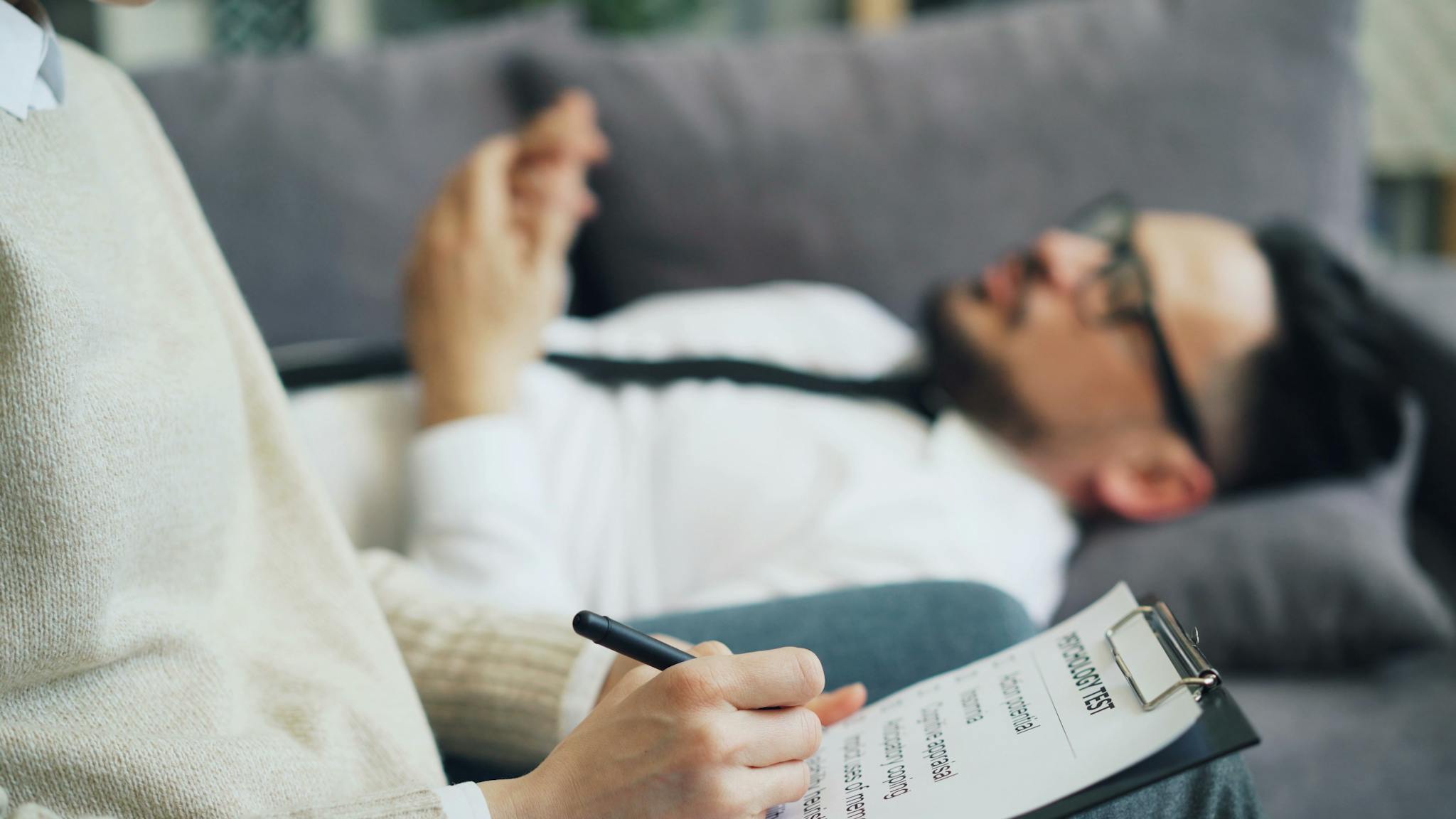 A client discusses issues during a therapy session with a therapist taking notes, indoors.